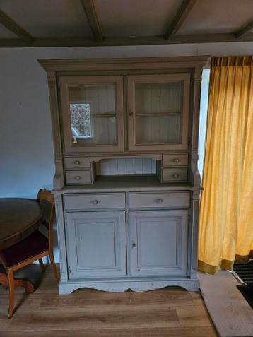 Grijze houten servieskast met glazen deuren.