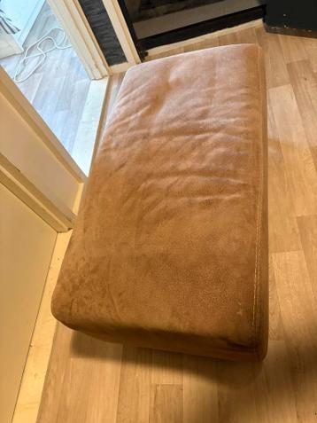 een bruine, rechthoekige poef met een suède-achtige textuur.