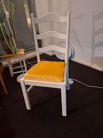 Twee witgeschilderde houten stoelen met gele kussentjes