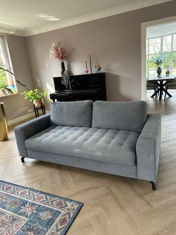 Grijsblauwe bank met gestoffeerde zitting en zwarte poten