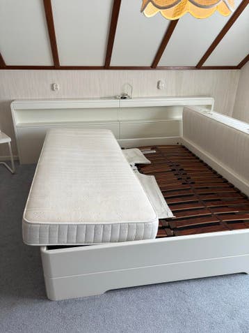 Wit tweepersoonsbed met lattenbodems en nachtkastjes