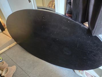 Ovale zwarte houten eettafel met zwart onderstel, gekruist.