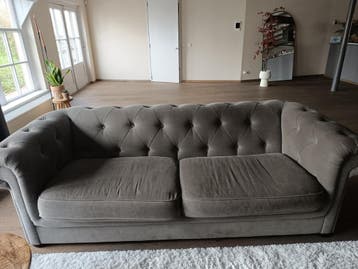 Stijlvolle grijze bank met diepe knopen en hocker