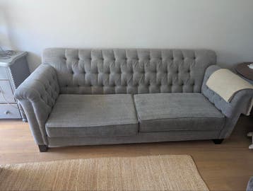 Leuke grijze bank met gecapitonneerde rug en armleuningen.