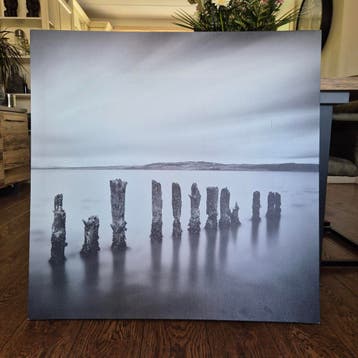 Zwart-wit canvas schilderij van palen in water