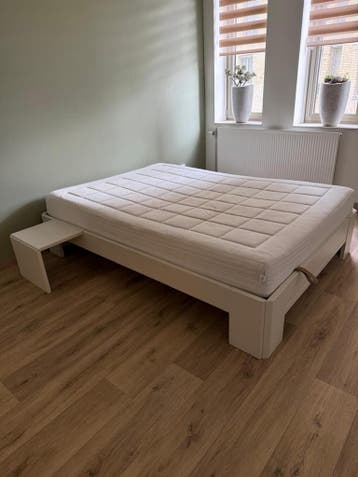 Wit tweepersoonsbed met matras en nachtkastje